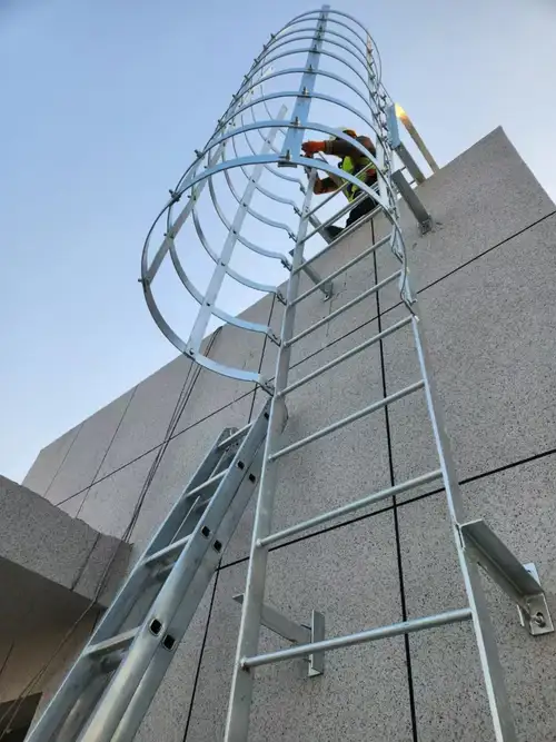 Escada marinheiro de aço com gaiola de proteção amarela instalada em estrutura industrial
